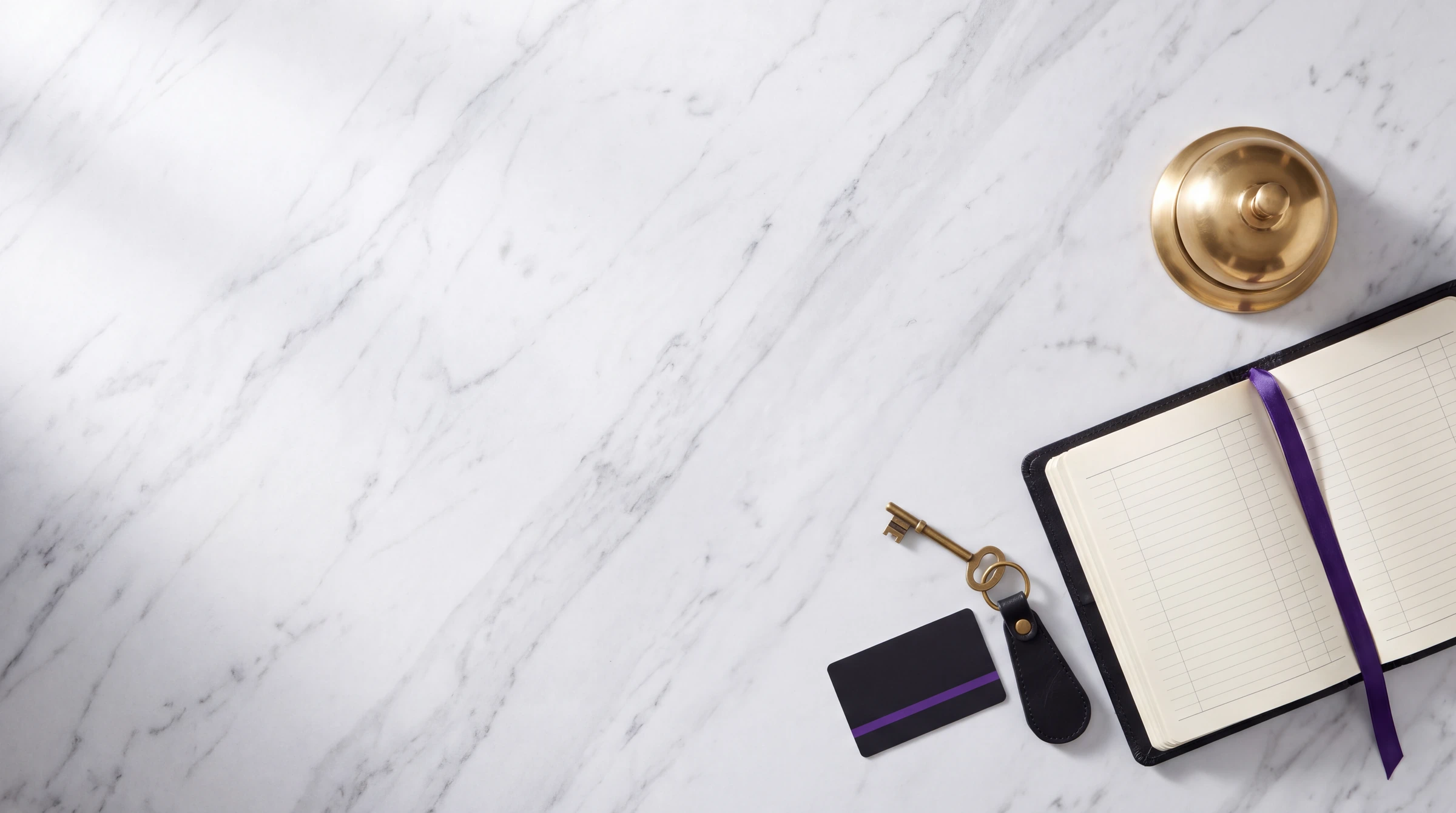 A brass reception bell, an open ledger and a room key on a white marble counter